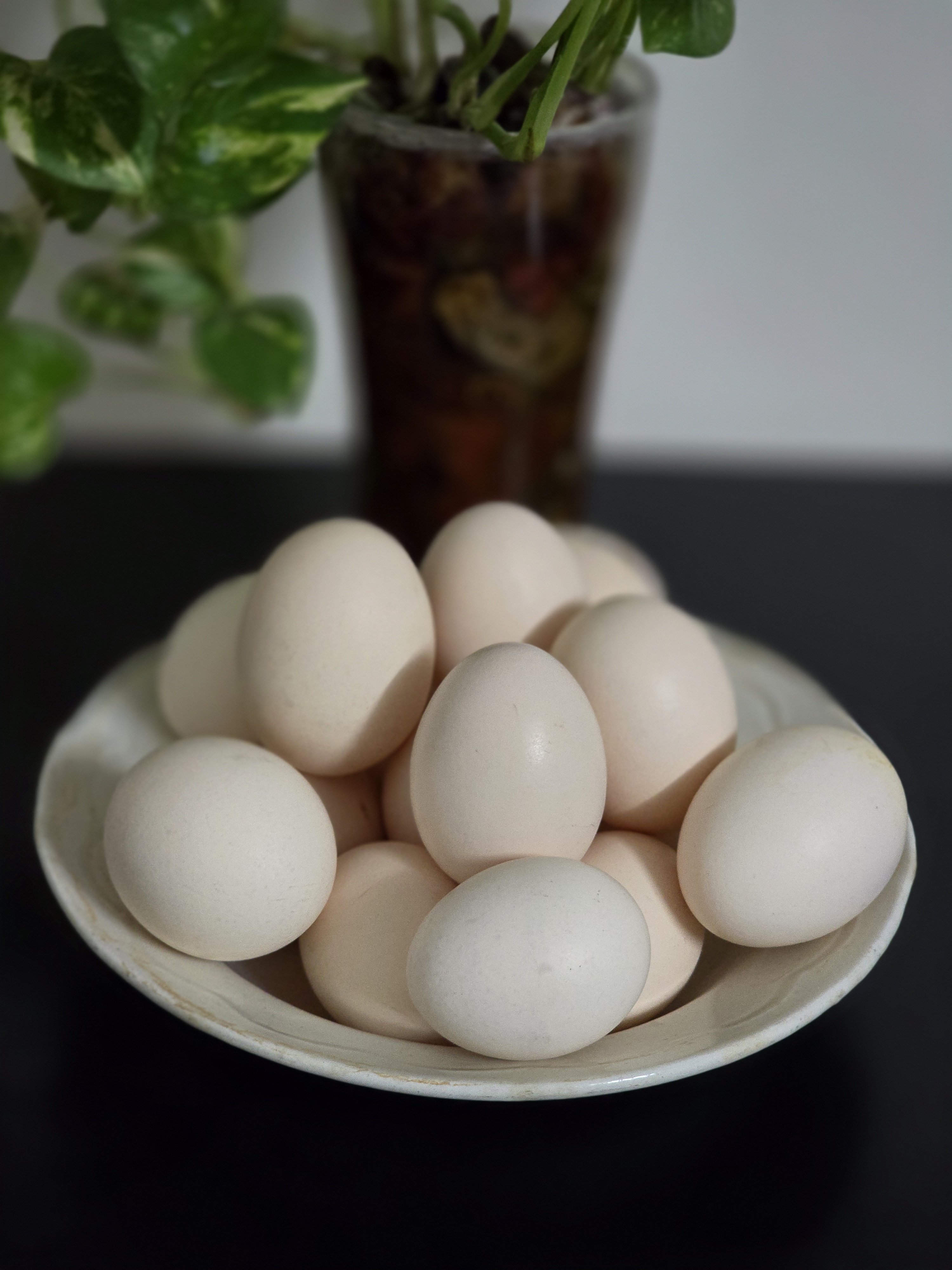 A bowl of pale, cream-shelled desi gavran eggs beside a leafy green plant